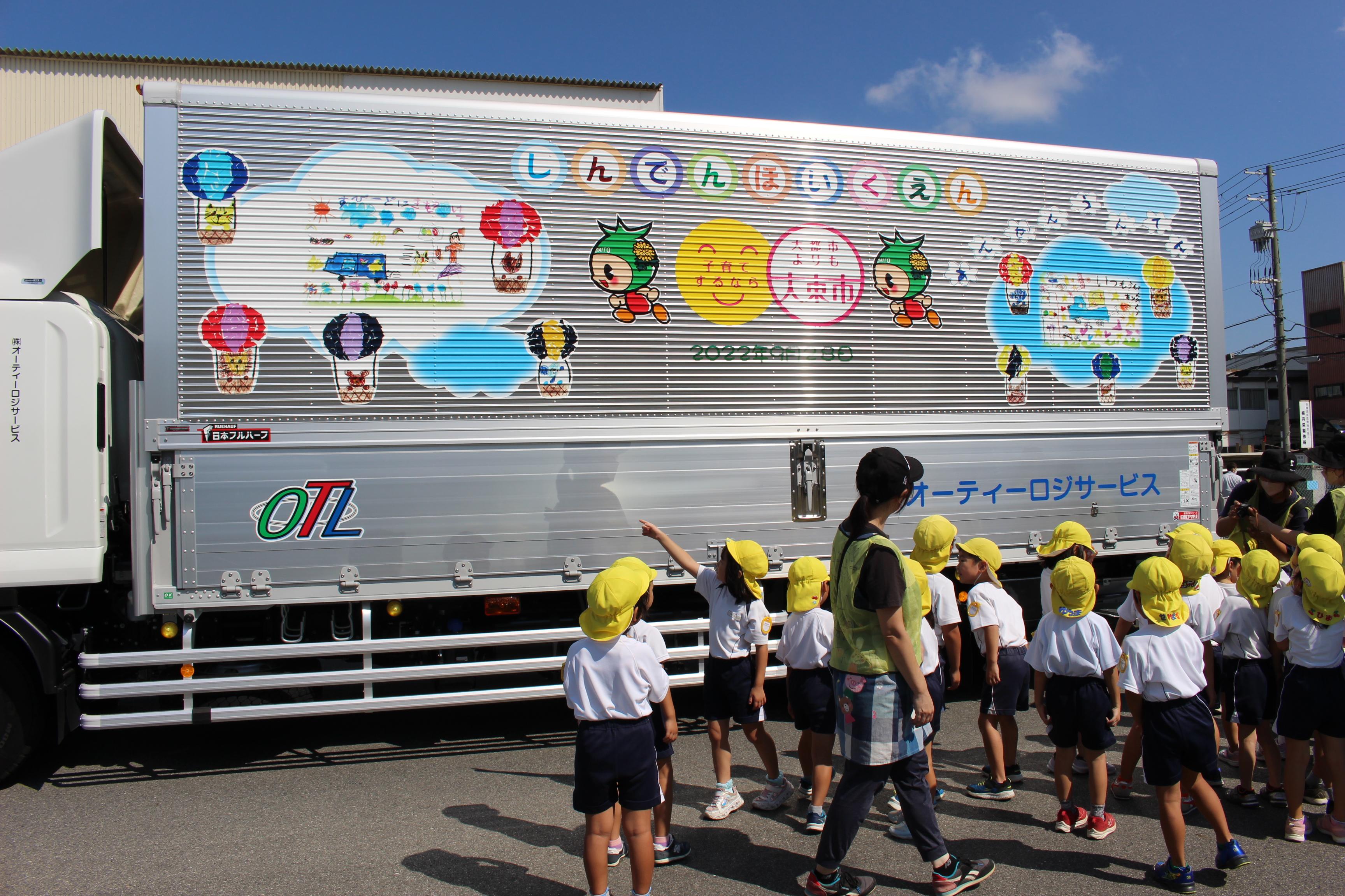 近所の保育園の皆さんに描いてもらった絵をラッピングしたトラックの納車式典の様子です。